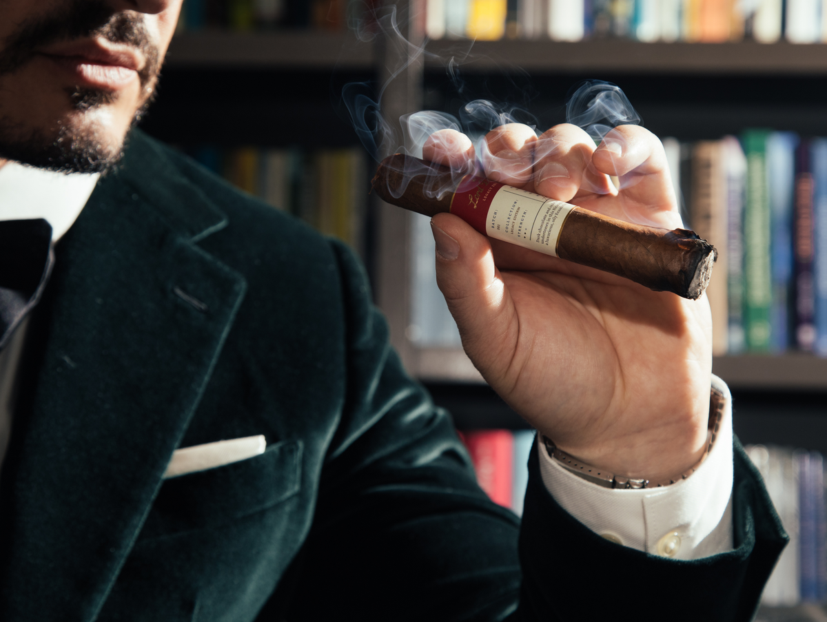 Man holding a smoking cigar in front of a bookshelf
