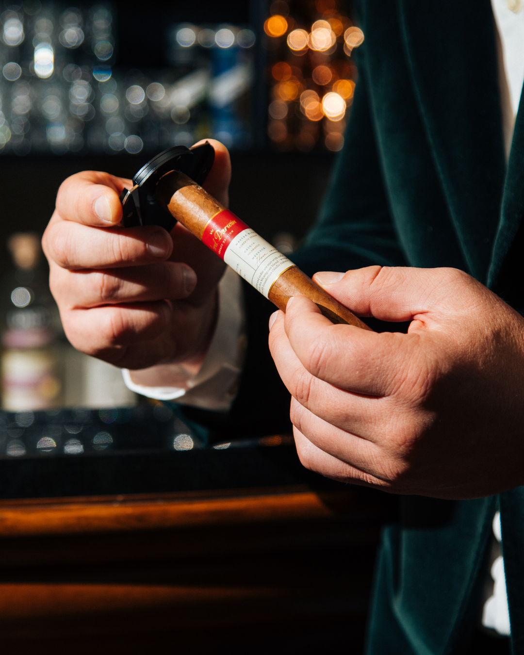 Person holding a cigar with a dark, blurred bar setting in the background